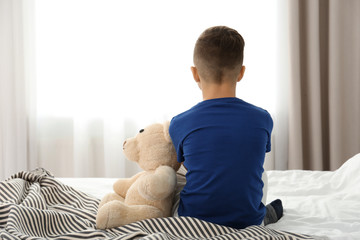 Lonely little boy sitting on bed in room. Autism concept
