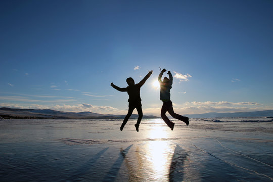 Silhouettes of happy young people jumping over the ice of lake Baikal at sunset.