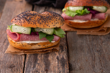 Sandwich with salami, fresh salad, cucumber on a wooden rustic background.