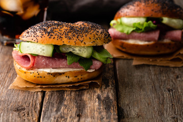 Sandwich with salami, fresh salad, cucumber on a wooden rustic background.