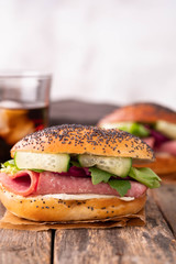 Sandwich with salami, fresh salad, cucumber on a wooden rustic background.