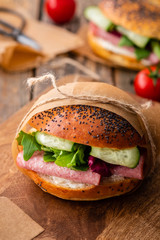 Sandwich with lettuce, fresh tomatoes, cucumber, ham, salami and cheese on a wooden background.
