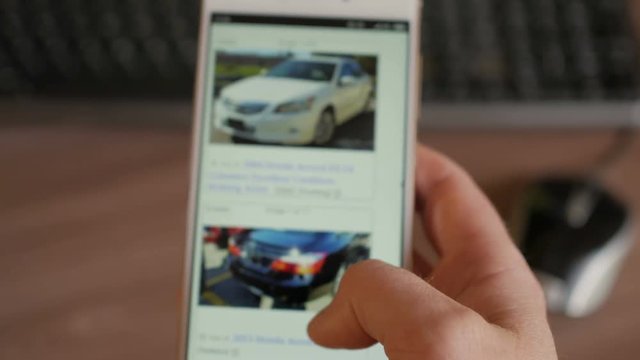 A man chooses to buy a car on the site. Looking at used vehicle to buy on a smartphone app. Close Up. Screen is blurred. 4K UHD.