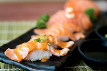 Mixed salmon sushi on black plate along with Japanese sauce and green leaf decoration, Japanese food, close up at sushi ..