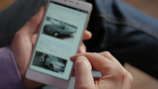 A man chooses to buy a car on the site. Looking at used vehicle to buy on a smartphone app. Close Up. Screen is blurred. 4K UHD.