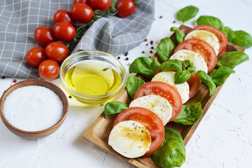 Mozzarella cheese with red tomatoes and basil leaves, pepper, olive oil, wooden desk, healthy food concept, white background