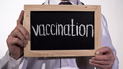 Vaccination written on blackboard in doctor hands, disease outbreak prevention