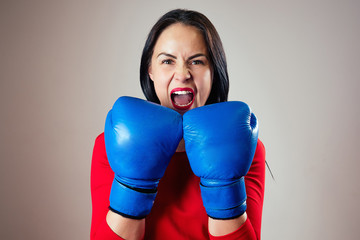 portrait of a beautiful brunette woman with a furious face with boxing gloves on her hands in the gym. athlete with makeup red lipstick boxing. Female power, feminism, screaming, rage, anger, power