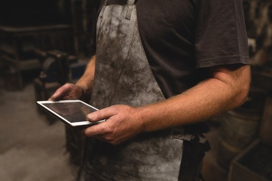 Blacksmith using digital tablet in workshop