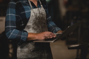 Blacksmith using laptop in workshop