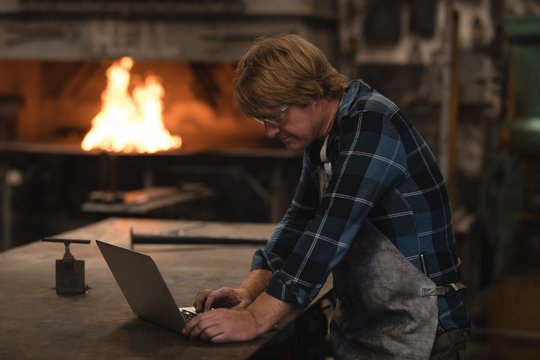 Blacksmith using laptop in workshop