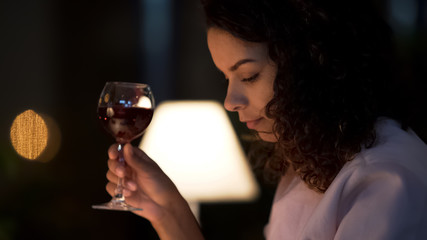 Biracial woman drinking wine in small restaurant, typing message on smartphone