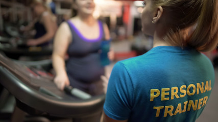 Overweight young woman asking personal training for advice on exercises in gym