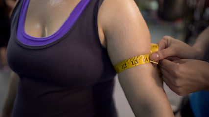 Trainer measuring womans arms after workout in gym, weight loss program results