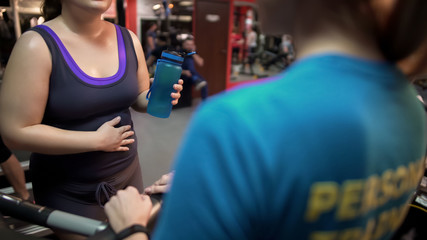 Pregnant woman consulting with personal trainer on pregnancy exercises in gym