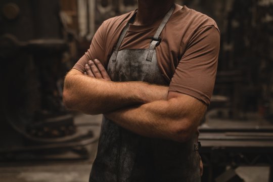 Blacksmith standing with arms crossed in workshop - Powered by Adobe