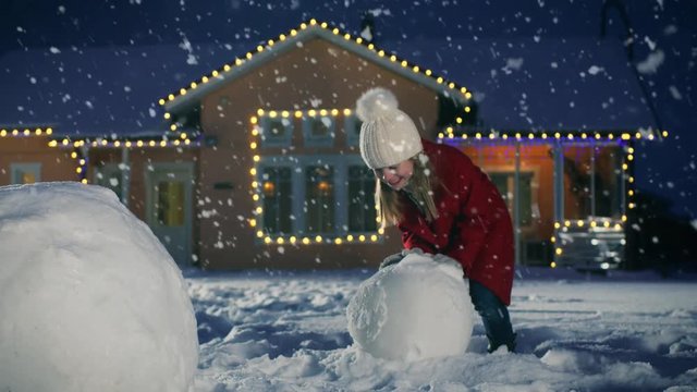 Cute Little Girl Making a Snowman, Rolling Snowball. Child Has Winter Fun,  Builds Snowman in the Backyard of Idyllic House with Garlands and Christmas Tree.