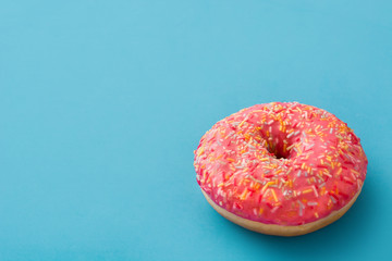 Pink frosted donut with colorful sprinkles on blue background. Copyspace