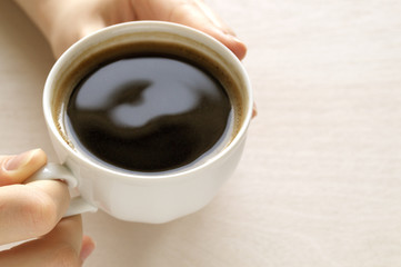Hands holding a Cup of coffee on a bright table.