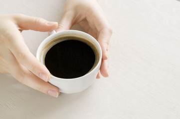 Hands holding a Cup of coffee on a bright table.