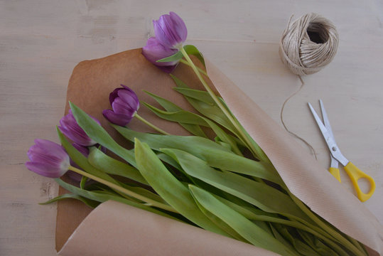 Overhead view of a bouquet of purple tulips, brown paper, string and scissors on a table