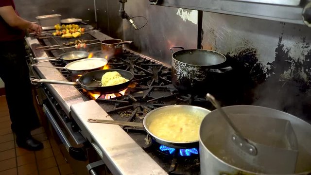Chefs on a cooking line in a restaurant kitchen moving pans and fire flashing.