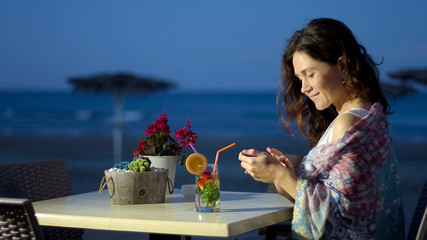 Beautiful lady using mobile phone at outdoor restaurant, smiling reading message © motortion