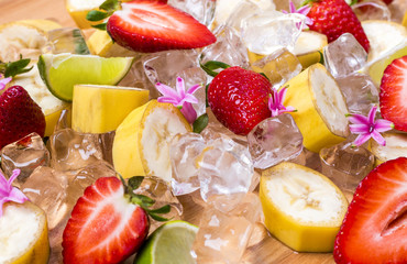 Pieces of fresh ripe fruits, strawberry, banana and lime in ice on wooden table, perfect snack for summer refreshment