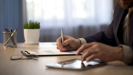 Company worker checking information on tablet to mark graphs, statistical report