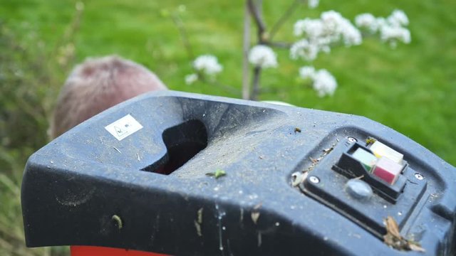 A man in the garden is laying wooden branches in the machine for shredding. Close Up