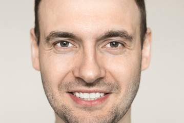 Handsome young man with a bristle smiling teeth. Portrait of a guy in a gray shirt on a light background.