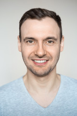 Obraz premium Handsome young man with a bristle smiling teeth. Portrait of a guy in a gray shirt on a light background.