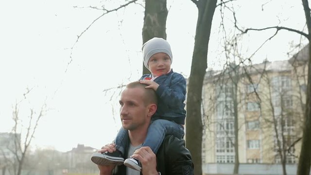 Funny little boy 1-2 years old sitting on dad's shoulders, father and son walking in a spring Park. Steadicam shot