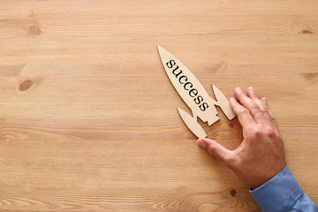 man's hand holding rocket with word - success - over wooden background.