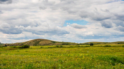 Green grass field on small hills and little mountain, blue sky with clouds