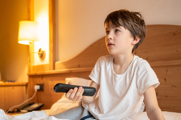Child on the bed watching TV holding the remote control
