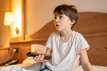 Child on the bed watching TV holding the remote control