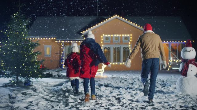 Lovely Young Family Running Towards Their Idyllic House, Everything is Decorated with Lights and Garlands for Christmas Eve. Father, Mother and Cute Little Daughter Have Fun. 