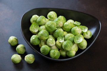 Fresh uncooked brussels sprouts in a black bowl, selective focus, studio shot