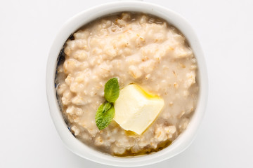 breakfast: oatmeal porridge with butter in white bowl on white background. Top view. Isolated