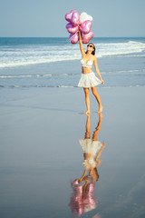 young and beautiful girl holding helium balloons air, running and jumping for joy at the sea....