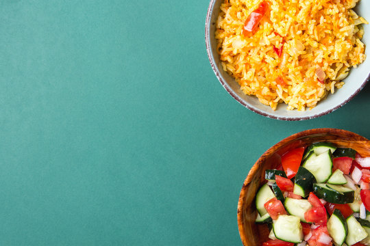 Traditional National Mexican Tomato Rice Stewed Pilaf with Hot Chili Peppers Garlic in Turquoise Bowl. Fresh Cucumber Onion Salsa Salad in Wooden Dish. Green Background. Top View Flat Lay. Copy Space