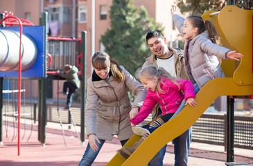 Obraz premium rodzice bawią się z córeczkami na zjeżdżalni na placu zabaw