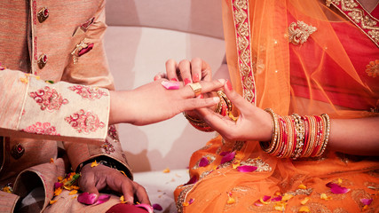 Indian bride putting a wedding engagement ring on finger of groom.