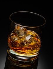 Glass of scotch whiskey with ice cube on a black background.