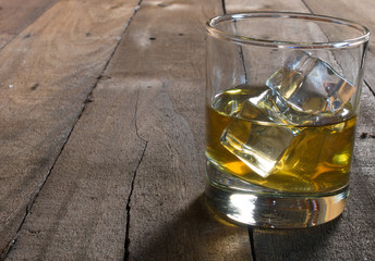 Whiskey in glass with ice cubes on wooden table