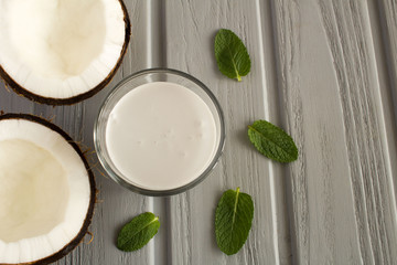 Coconut  milk in the glass and halves of coconut on the grey wooden  background.Top view.