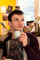 young guy trying to drink espresso on the palate in a coffee house holding a cup and a plate