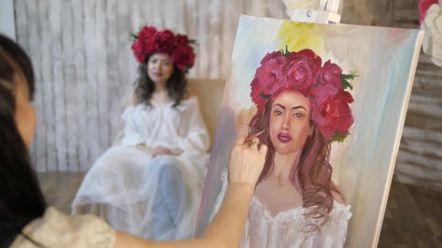 artist draws a portrait from nature. The artist draws a portrait from nature. Floating camera focus, camera in motion. Beautiful model, with a wreath of scarlet peonies on his head, posing sitting in