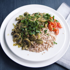 Red rice with mushrooms and cherry tomatoes. Vegan dish. European cuisine. Simple healthy lunch. Vegetarian rice dish on the white plate. Close up. Toned photo.
